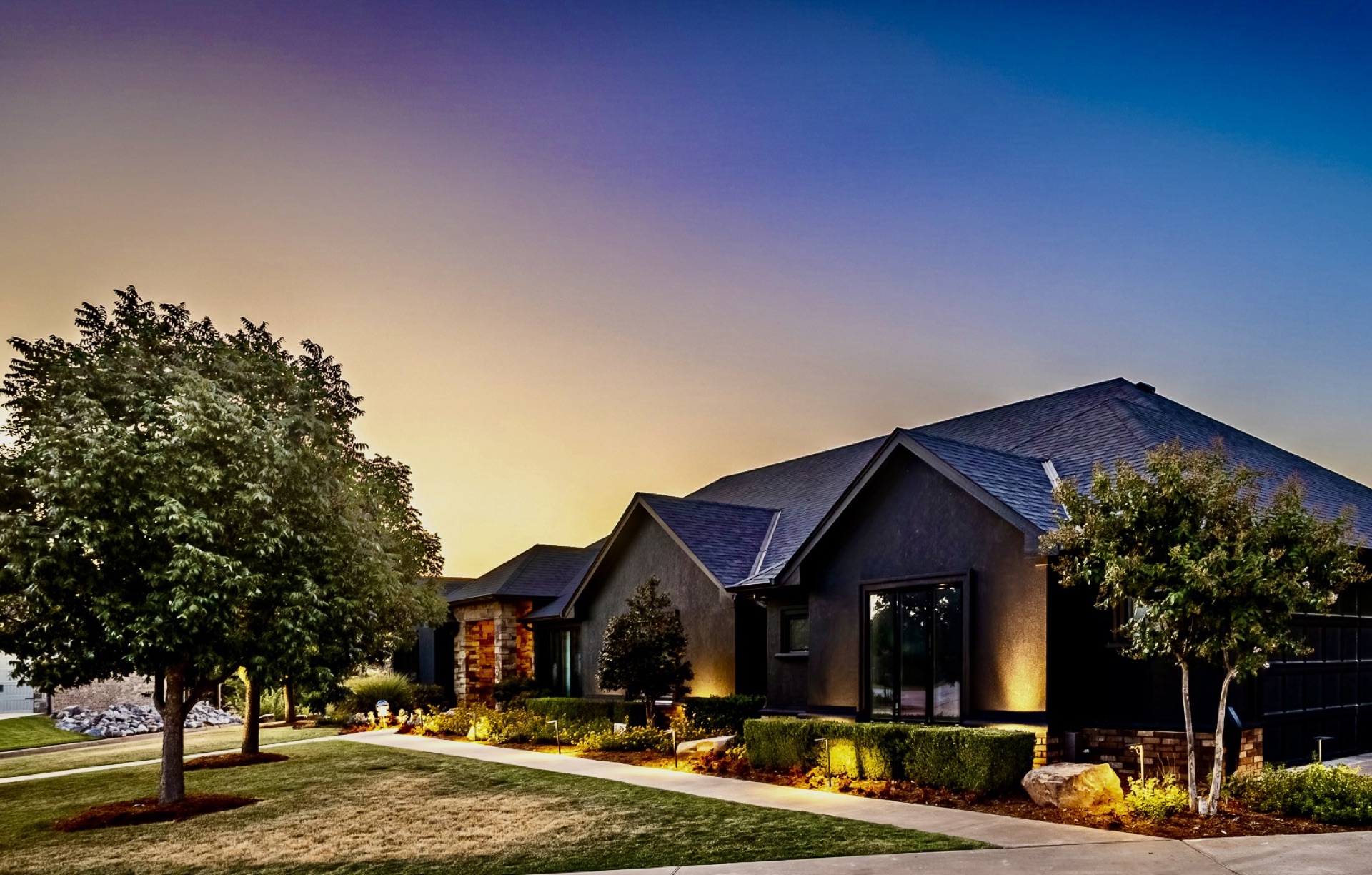 Home exterior with professional landscape lighting illuminating the walkway and beds at dusk